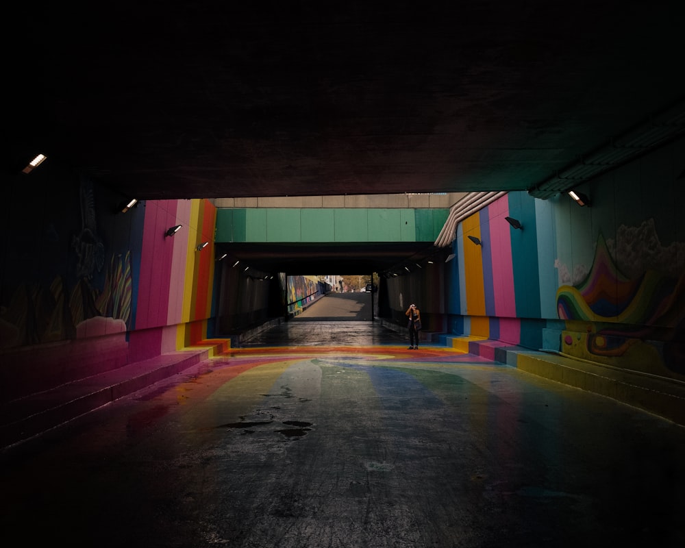 Una persona parada en un túnel con una pared pintada con arco iris