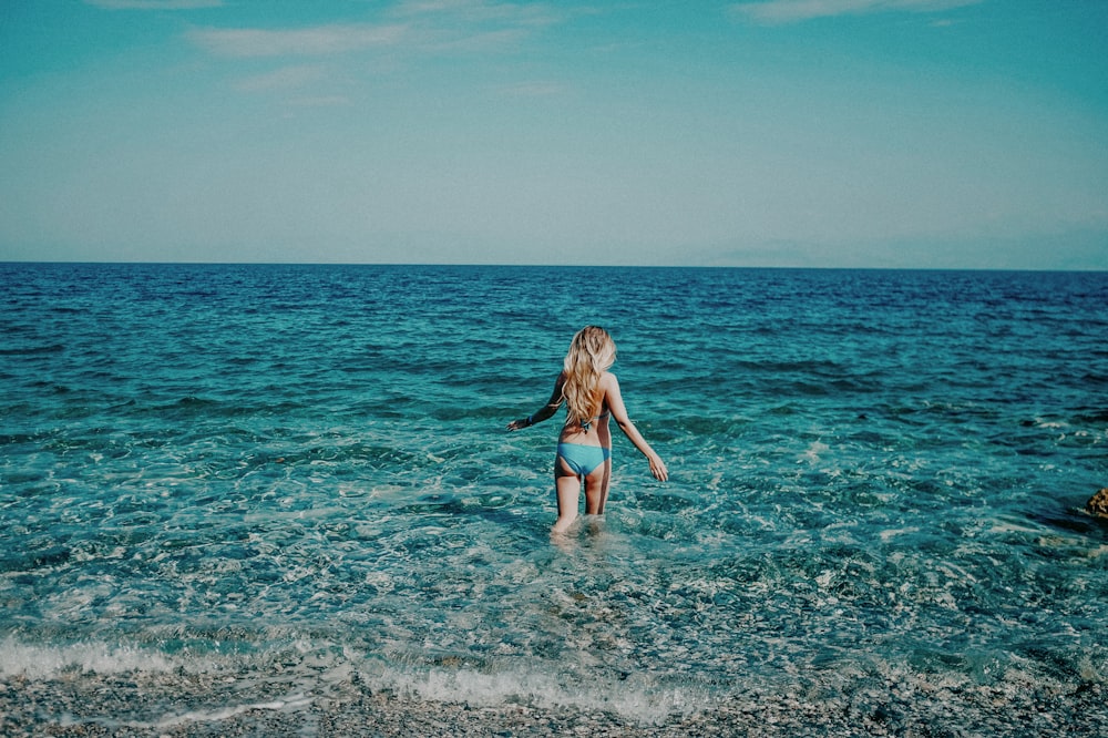 Una chica en bikini azul vadeando en el océano