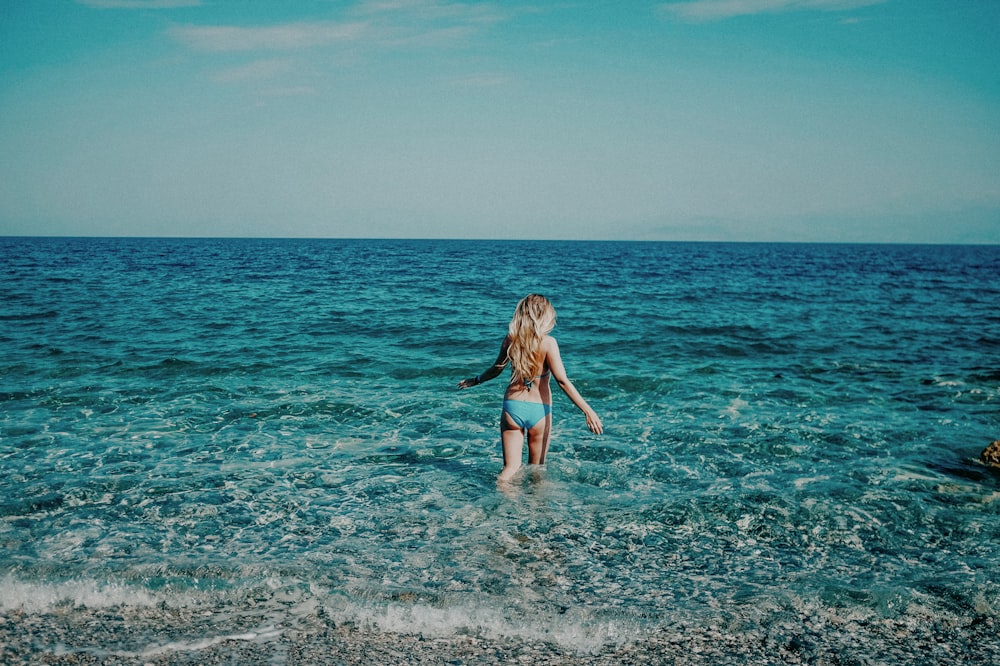 a girl in a blue bikini wading in the ocean