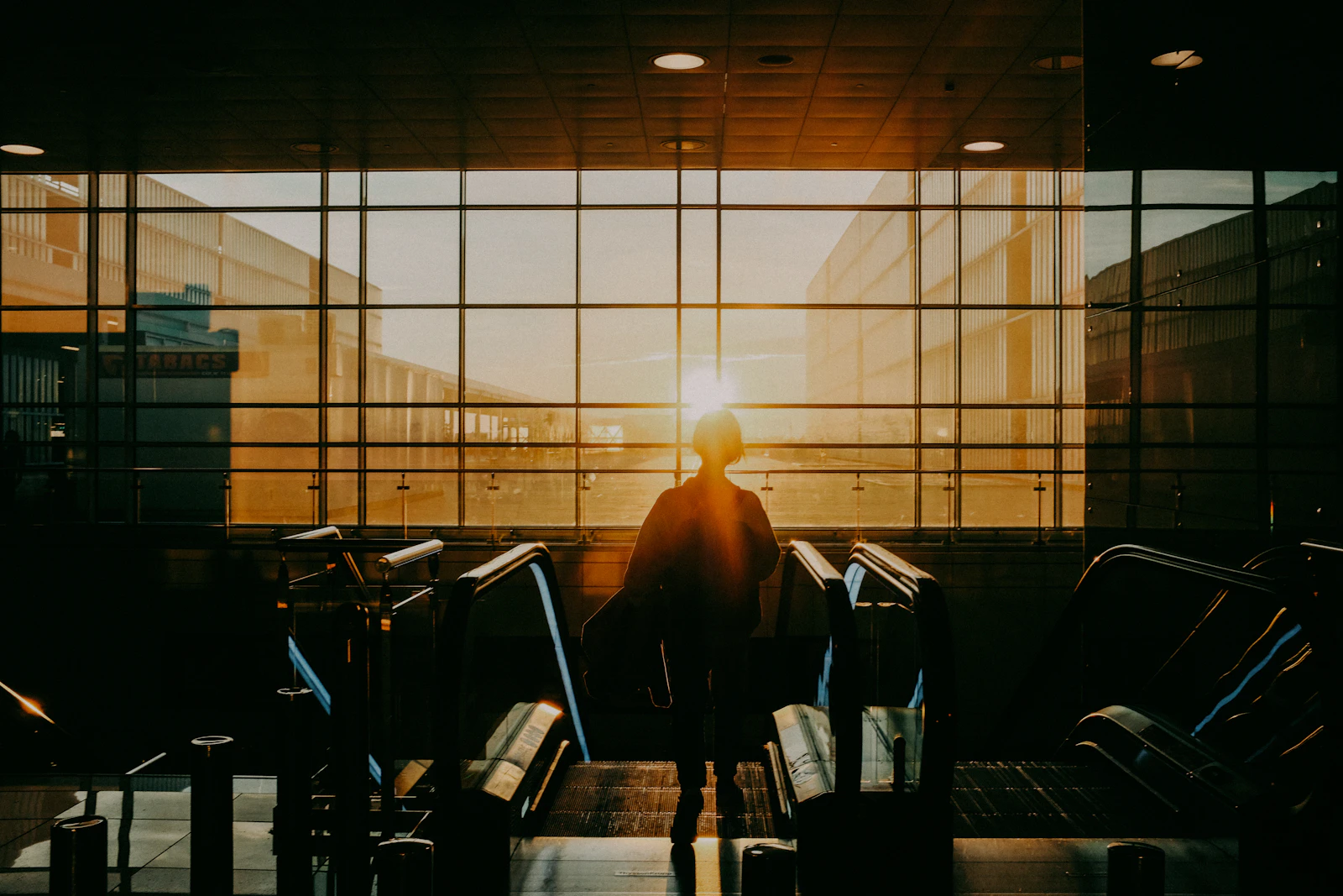 Silhueta de uma viajante diante da janela de um aeroporto ao nascer do sol, a caminho do intercâmbio