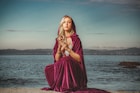 a woman in a purple dress sitting on a rock by the water