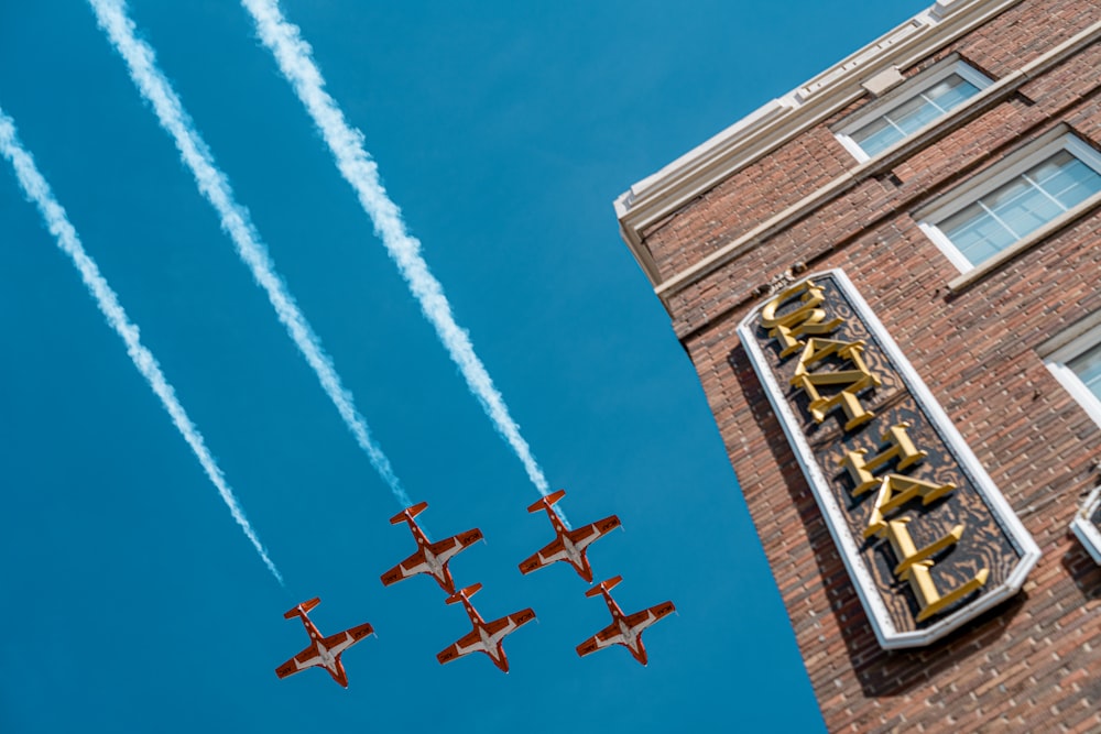 four airplanes flying in formation in front of a building