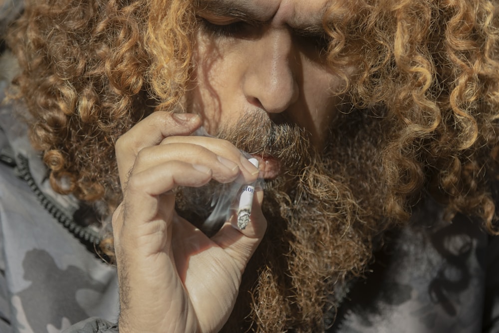 a man with long curly hair is smoking a cigarette