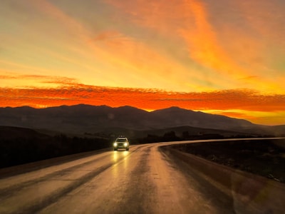Dynamic shot of a sports car speeding on a winding mountain road at sunset.
