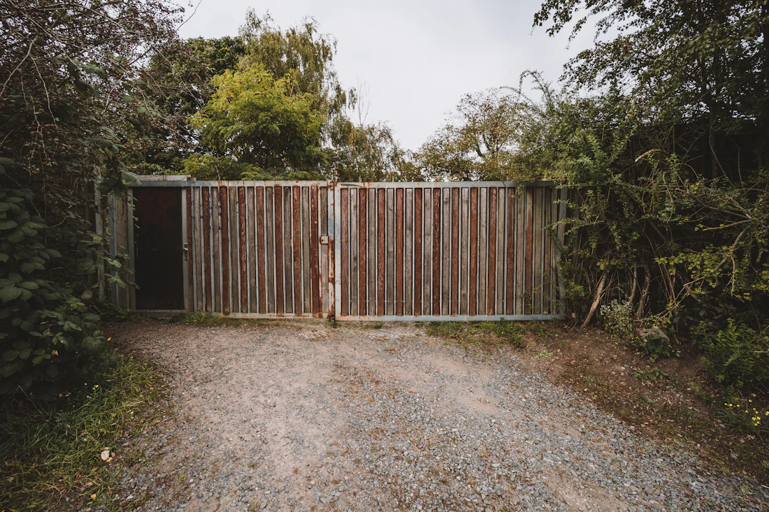 Tall wood driveway gate at the end of a gravel drive