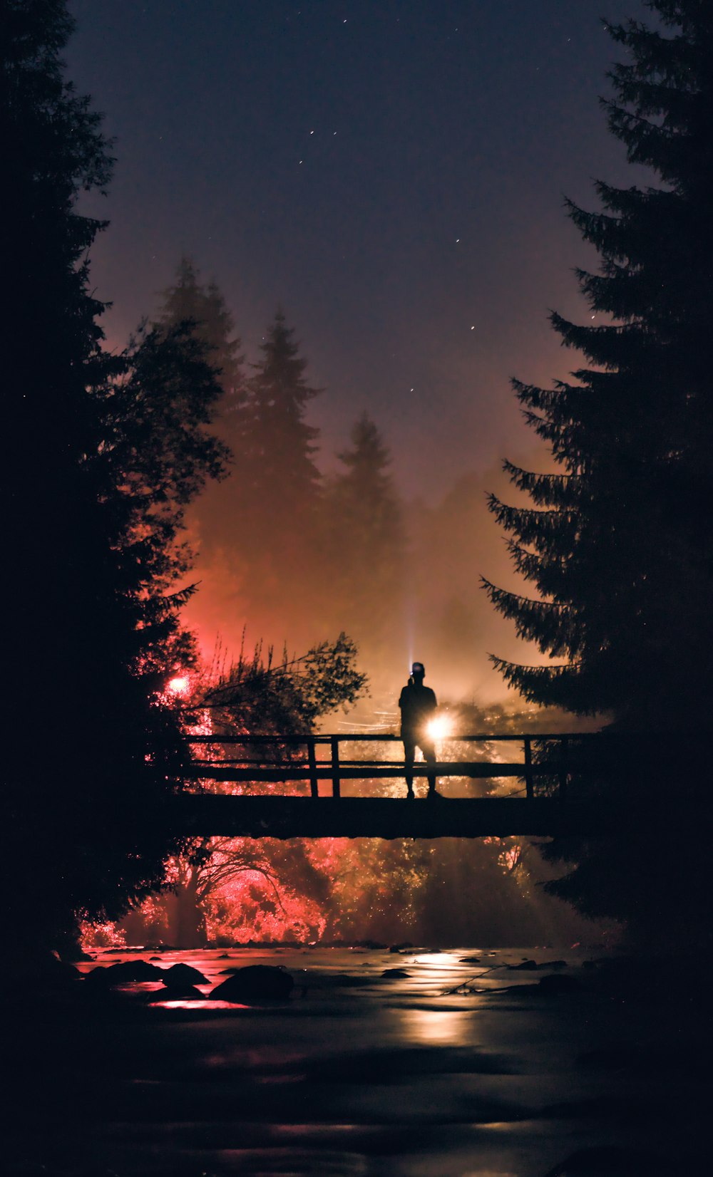 a man standing on a bridge over a river at night