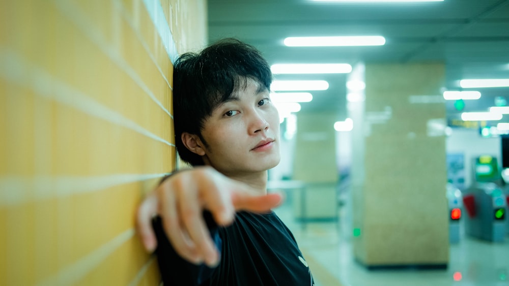 a young man leaning against a wall pointing at something