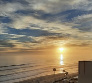 A vibrant sunset over a tropical beach with a plane flying low in the distance