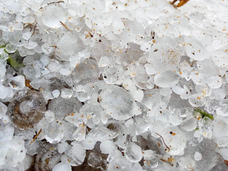 A close-up of a damaged roof with hailstones scattered around, highlighting the impact of a recent storm.