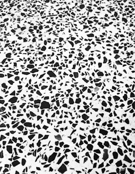 A black and white terrazzo pattern with irregular, randomly distributed black stone-like fragments set in a white matrix.