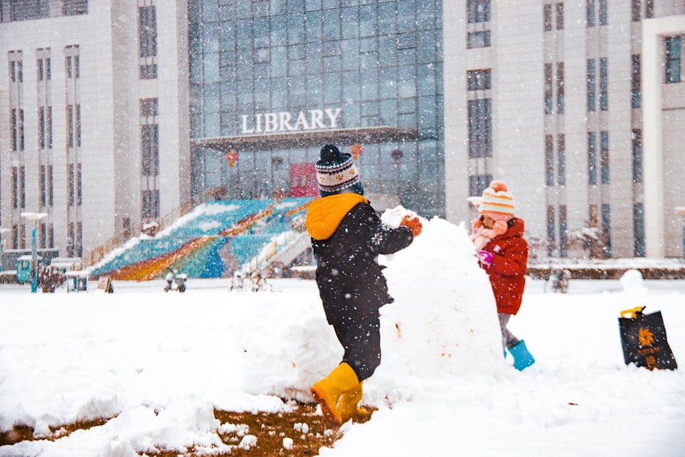 two children playing in the snow in front of a library