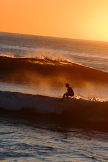 A surfer catching a glowing wave at sunset, the sky painted in warm oranges and purples