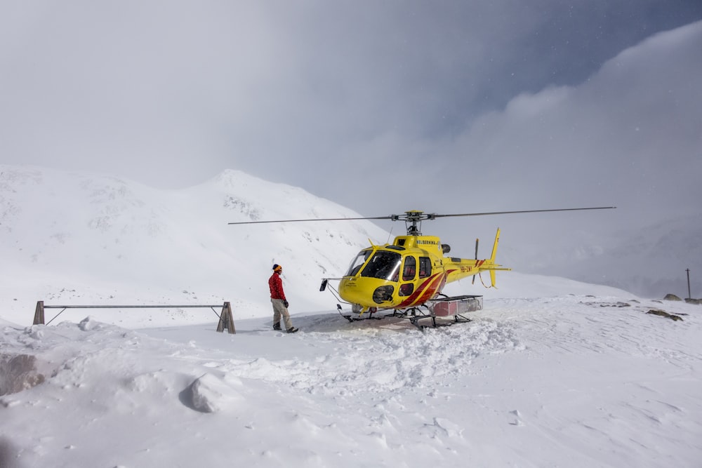 a man standing next to a helicopter on top of a snow covered mountain