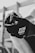 A close-up in black and white captures a hand wearing a glove labeled 'TEN Protection Superthin.' The hand is holding an object, possibly a can, with a blurred background indicating an outdoor or construction setting.