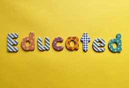 Various letters spelling out the word 'Educated' on a yellow background. Each letter is uniquely designed with different patterns and colors.
