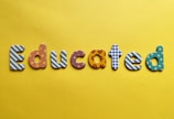 Various letters spelling out the word 'Educated' on a yellow background. Each letter is uniquely designed with different patterns and colors.