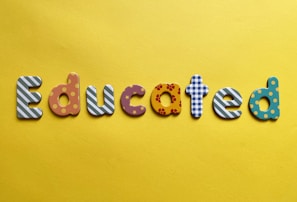 Various letters spelling out the word 'Educated' on a yellow background. Each letter is uniquely designed with different patterns and colors.