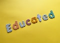 Colorful letters spelling the word 'Educated' are arranged on a bright yellow background. Each letter features a different pattern, such as stripes, polka dots, flowers, and stars.