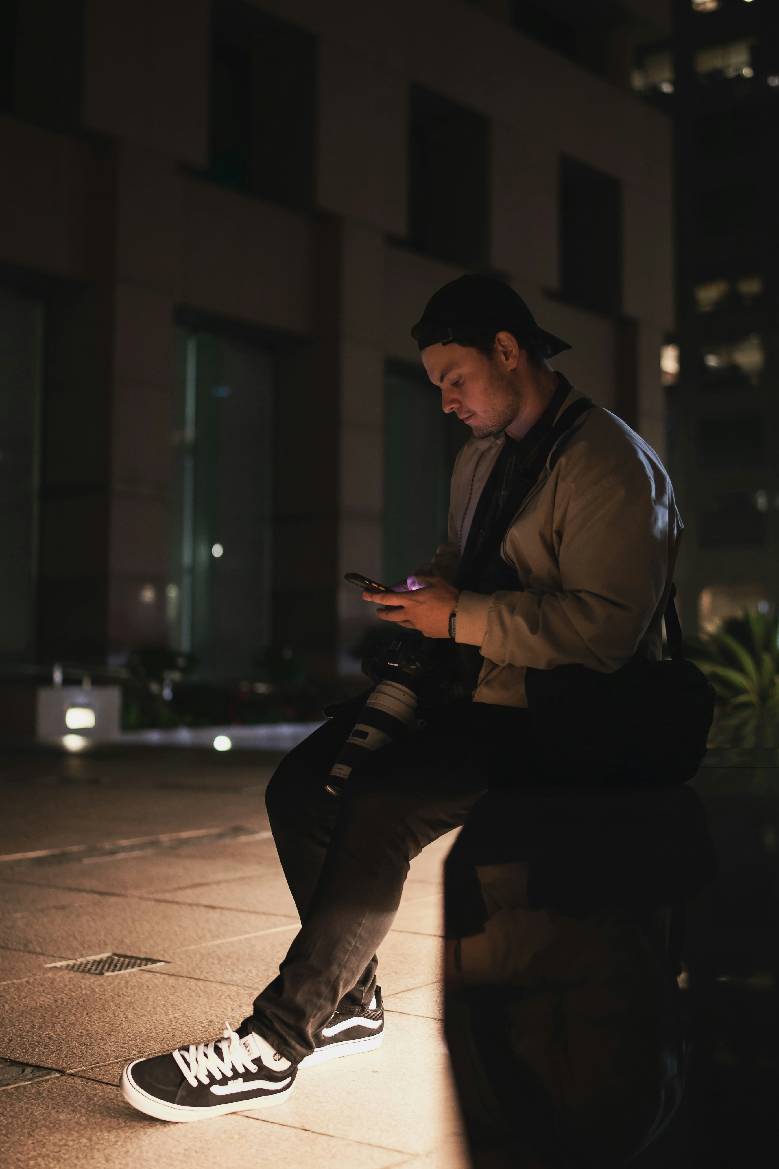 A man sitting on a ledge looking at his cell phone photo – Free Person ...