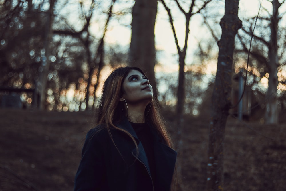 a woman standing in a forest looking up at the sky