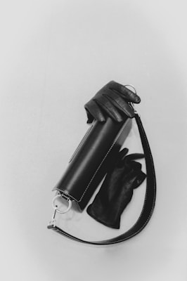 A sleek, cylindrical leather handbag is paired with matching black leather gloves. The bag features a silver clasp and a strap, adding a touch of elegance.