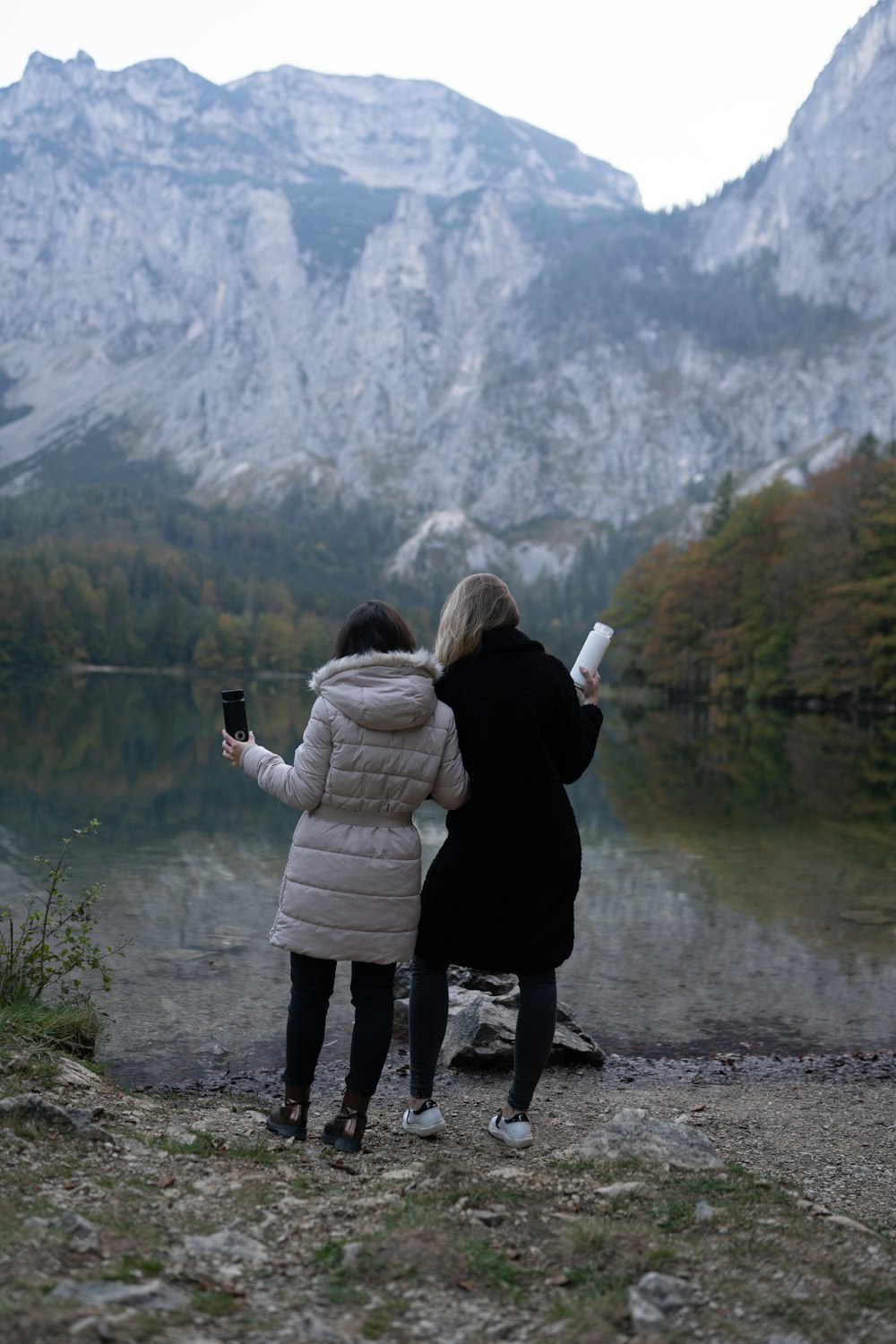 a couple of women standing next to a lake