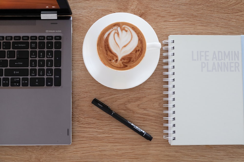 a cup of coffee on a saucer next to a laptop