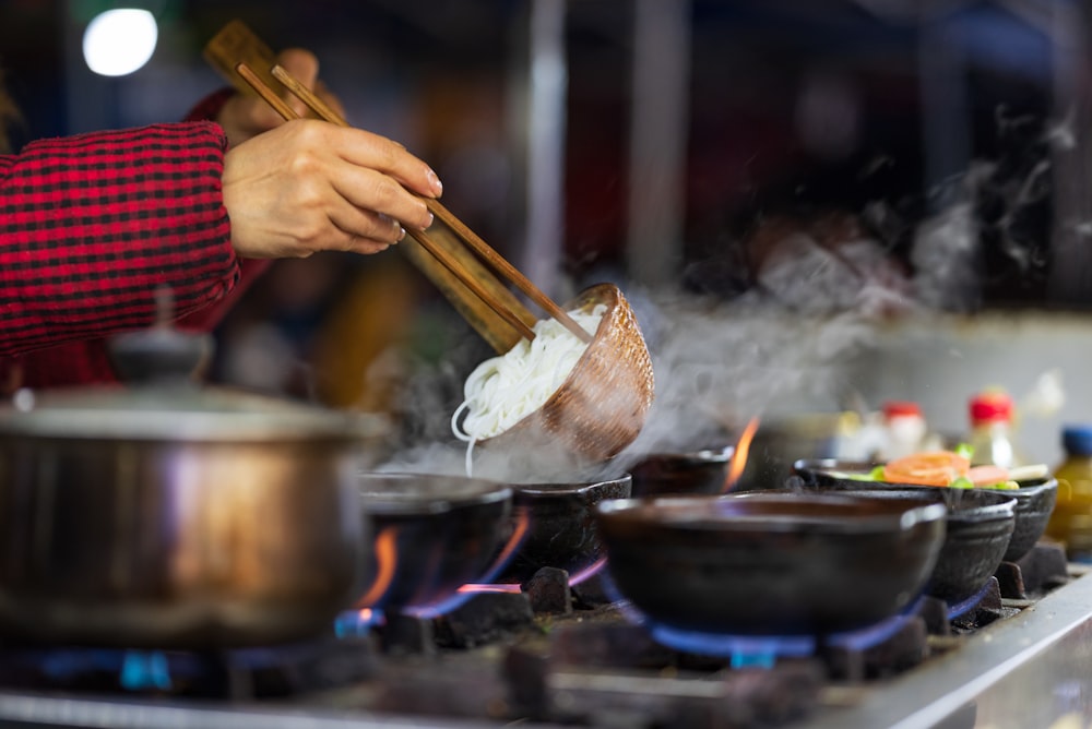 a person cooking food on a stove with chopsticks