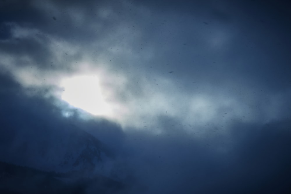 a bird flying through a cloudy sky with a mountain in the background