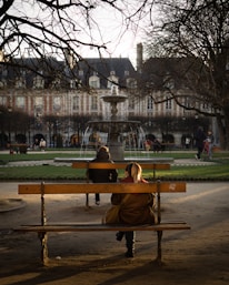 two people sitting on a bench in a park