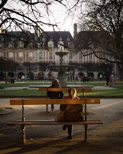 two people sitting on a bench in a park