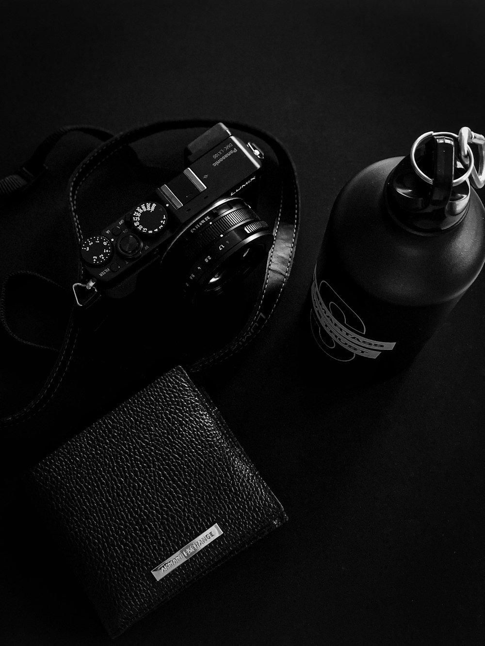 a camera, wallet, and bottle on a black surface
