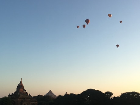A happy family waving from a colorful hot air balloon floating gently over Delhi's skyline at sunrise.