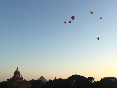 A hot air balloon drifting gracefully over the Karnak Temple at sunrise, bathed in golden light.