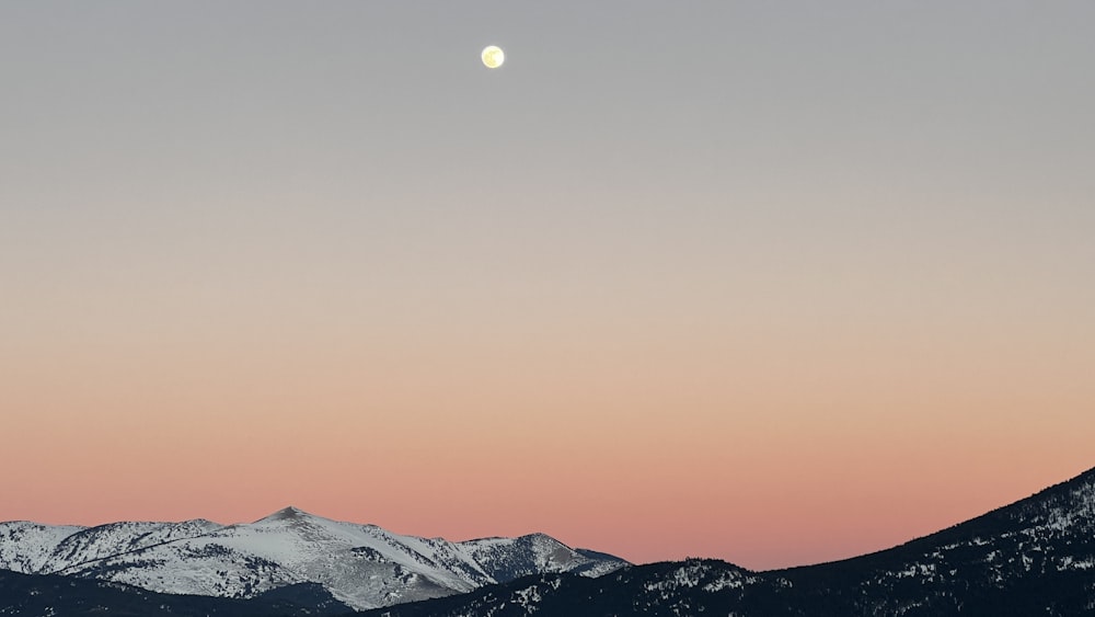 the moon is setting over a mountain range