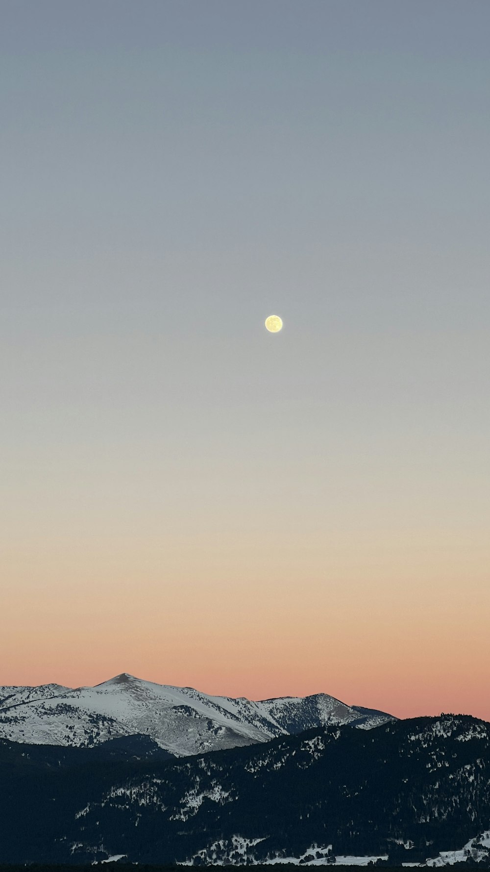 the moon is setting over a mountain range