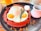 A vibrant red waffle topped with a sunny side up fried egg, garnished with rosemary, pecans scattered around the plate, and accompanied by a small cup of syrup and a dollop of cream.