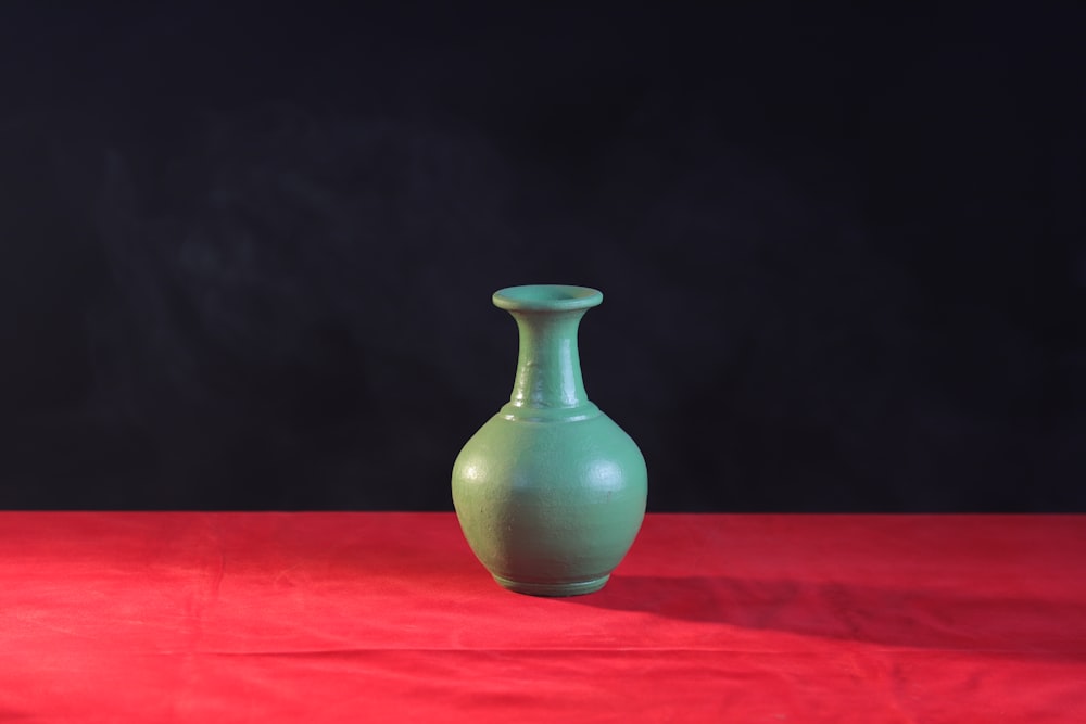 a green vase sitting on top of a red table