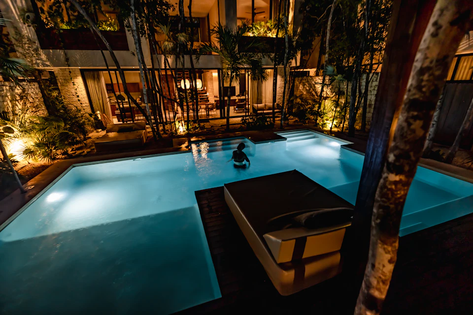 Two large swimming pools at night with person sitting on lounge chair near pool edge