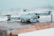 A compact, modern drone is resting on a wooden surface dusted with snow. The drone is gray and streamlined, with extended rotor arms and visible camera components. The background is softly blurred, suggesting a cold outdoor environment.