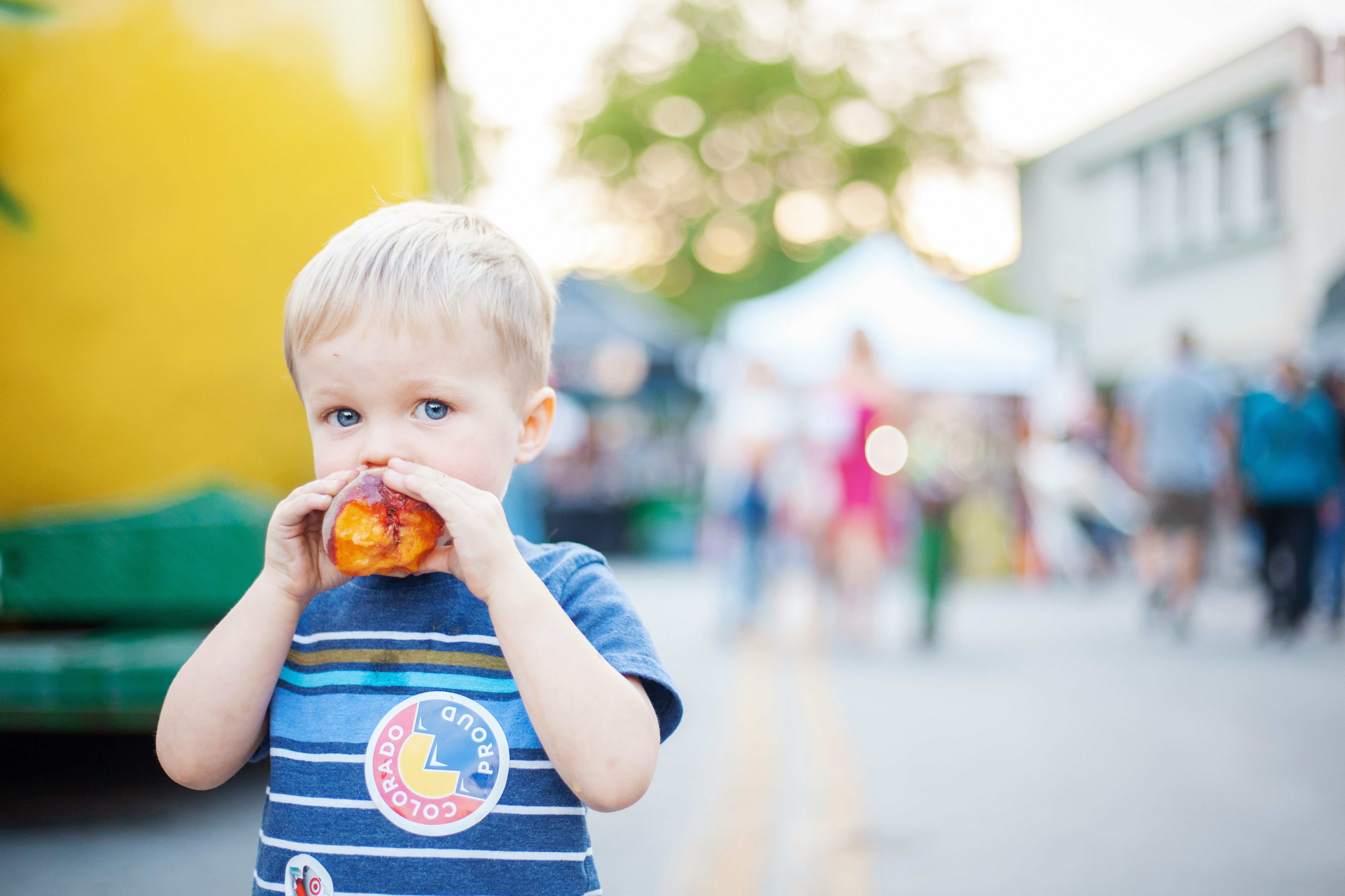Little boy eating a peach at a family farmers market in Colorado.