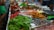 A colorful assortment of dried fruits and snacks is displayed on a market stall. There are trays filled with vibrant green kiwi slices, bright red cherries, and other assorted dried fruits in various shades of red, orange, and brown. Alongside the trays are some electronic scales, suggesting this is a place where items are sold by weight. The setup is neatly arranged, and the fruits have a glossy appearance.