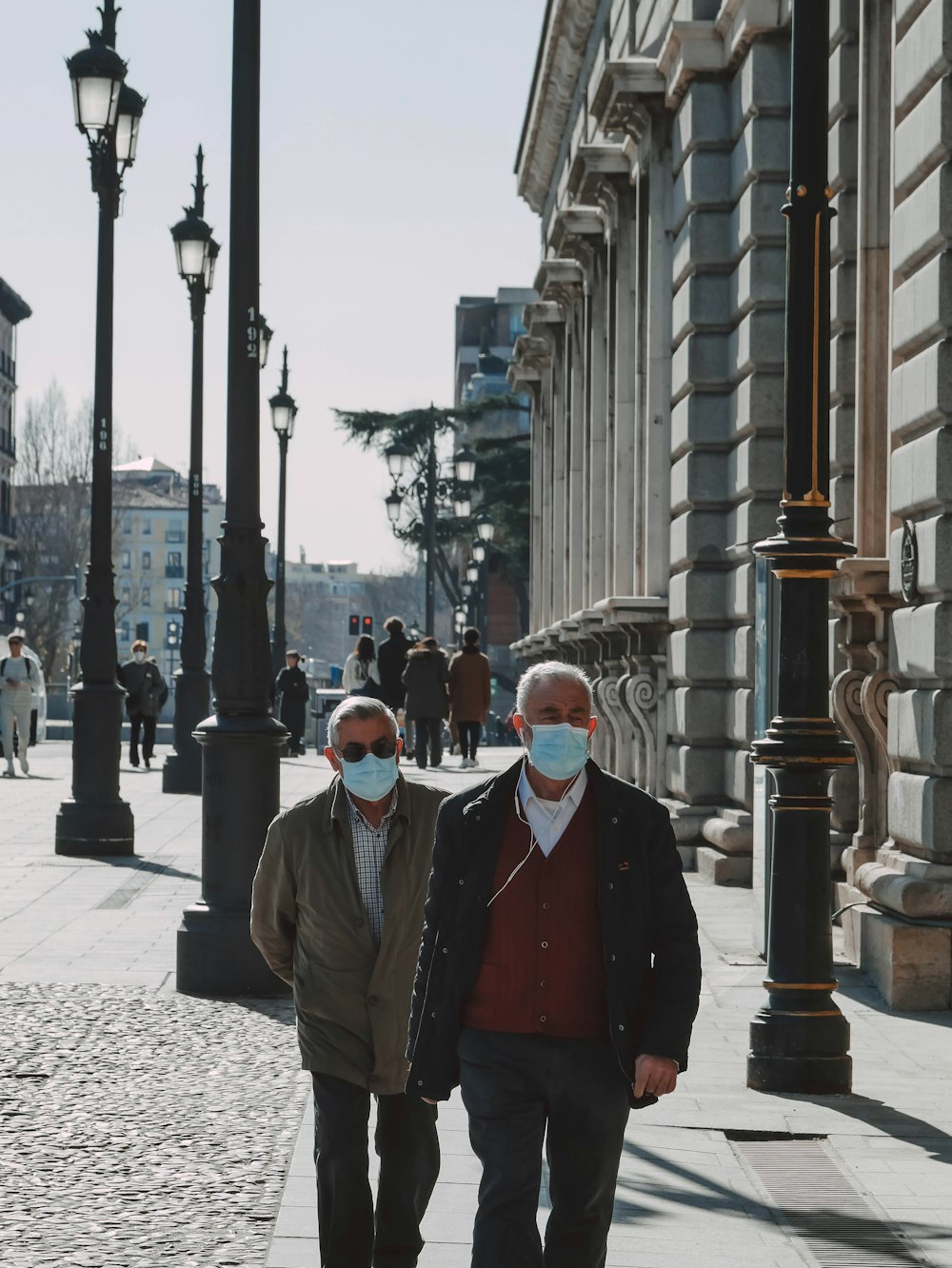 two men walking down a sidewalk wearing masks