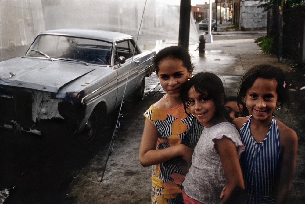 a little girl standing in front of a car posing for the camera