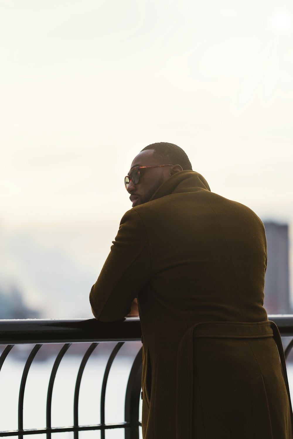 a man in a brown coat leaning on a railing