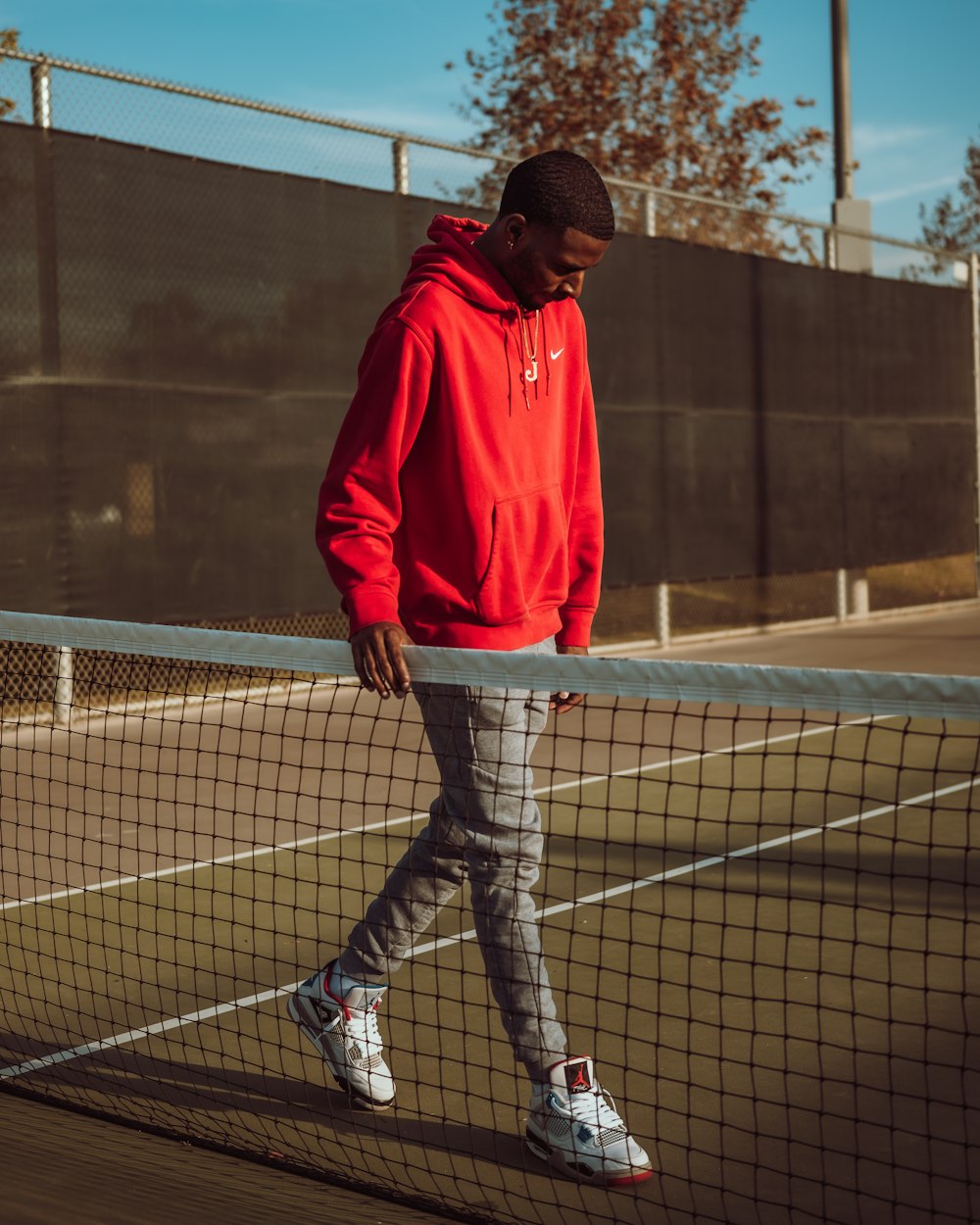a man in a red hoodie is walking on a tennis court
