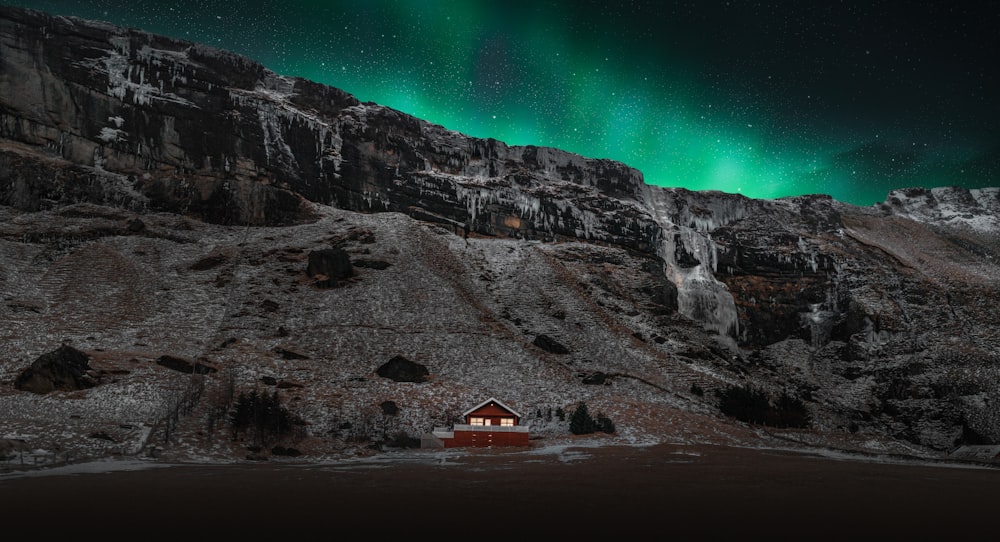 Una cabaña en medio de una montaña bajo una luz verde de aurora