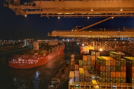Cargo ship loaded with containers leaving a bustling port at dawn, symbolizing global trade.