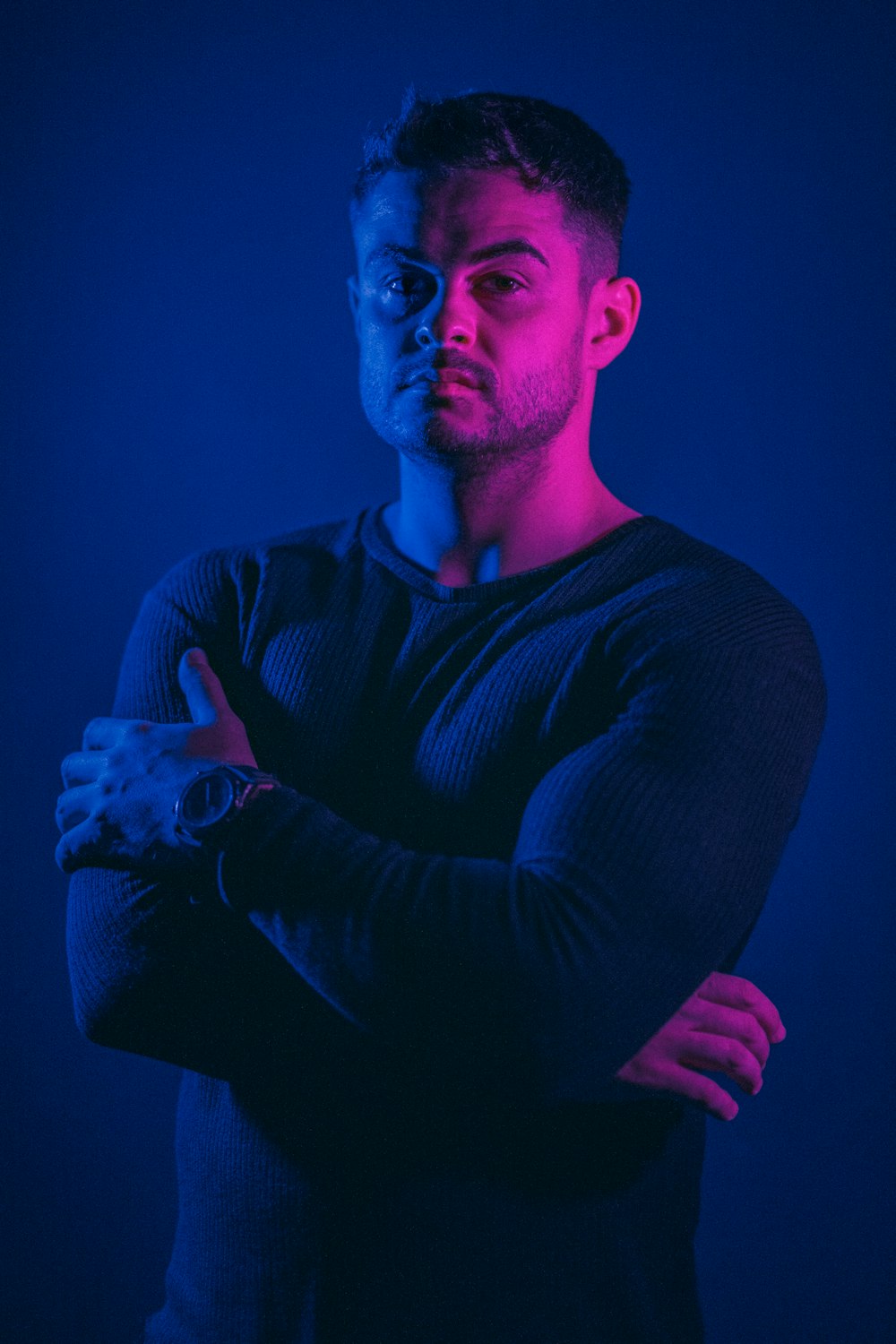 a man standing with his arms crossed in front of a blue background