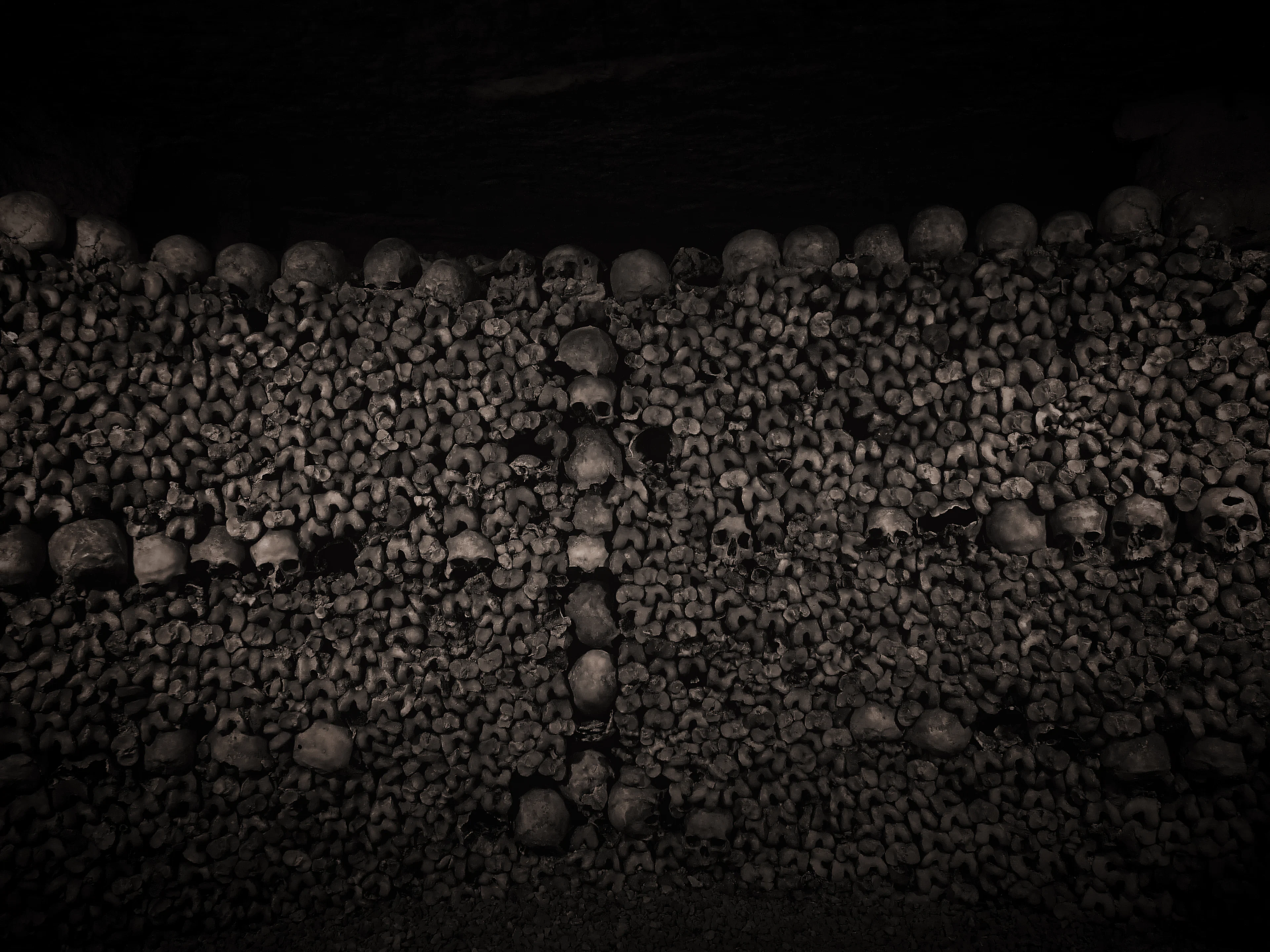 An ossuary wall in the Paris Catacombs of stacked femurs with rows and a cross of skulls
